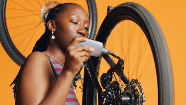 BIPOC mechanic using specialized glue to fix damaged bicycle chain, orange studio background. Expert applying adhesive on bike parts during checkup process, close up shot