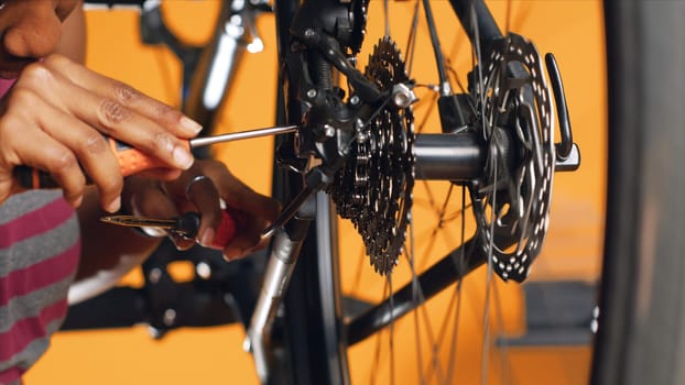 Technician pushing pedals to rotate bike wheel, inspecting it, using screwdriver and hex socket wrench to fix it, close up shot. Professional testing bike crank arm and chain rings, studio background