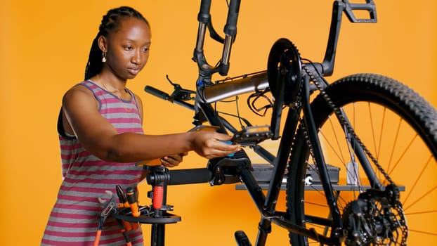 Engineer with tablet in hand analyzing damaged bike over studio background awaiting repair and maintenance. Woman using electronic device to diagnose bicycle on repair stand, camera B