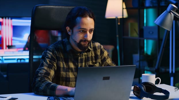 Freelancer sitting at home office desk and typing on laptop keyboard, doing his job. Remote worker using electronic device to send emails to customers from living room, camera A