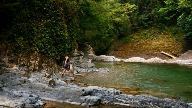 Man walking on the rocky river in paradise place. Creative. Woman cooling her feet in cld mountain stream