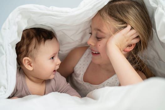 Little girl and her newborn brother hiding under the blanket