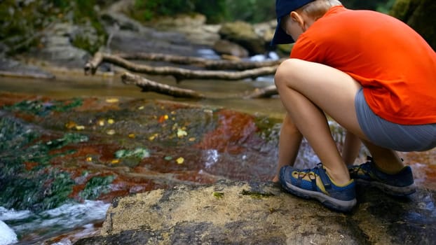 Tourist boy puts his hands in the river to drink cold clear water. Creative. Young boy drinking water from spring