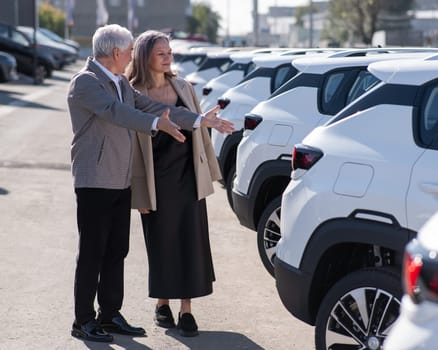 Mature Caucasian couple walks past cars outdoors, choosing a new one