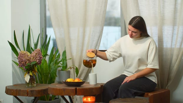 Young woman enthusiastically drinks tea in cafe. Media. Young woman drinks warming tea in cozy cafe by window in winter. Warming tea in cozy cafe on winter day.