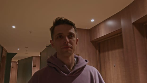 Young man walking in corridor of hotel building. Stock clip. Man in a hall wearing hoodie