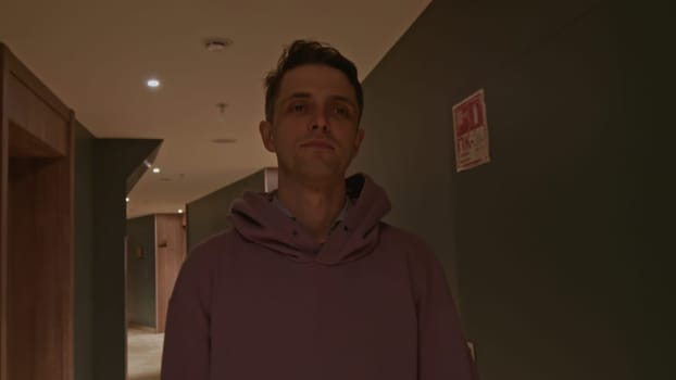 Young man in pink oversize hoodie at the hotel. Stock clip. Man walking along room doors in long corridor