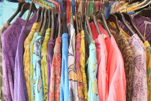 Vibrant assorted garments hanging on a clothing rack in a shop, showcasing various colors and patterns.