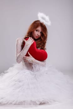 Pretty young girl dressed as angel posing with heart