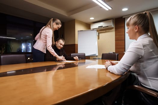 Businesspeople taking deal. Businessman signing contract after making agreement while his female partner sitting in front of him