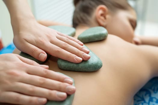 Massage therapist puts spa stones on girl's back, close-up