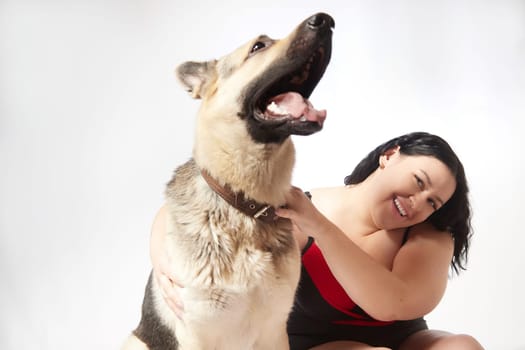 Portrait of attractive thick woman in red black swimsuit with big dog shepherd on white background. Body positive, selfie of Funny plus size model