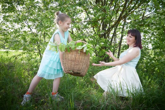 Happy mother and daughter enjoying rest, playing and fun on nature on a green lawn and with blooming apple tree in the background. Woman and girl resting outdoors in summer and spring day