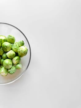 Fresh Brussels sprouts in a glass bowl on a white surface with copy space, healthy eating concept. High quality photo