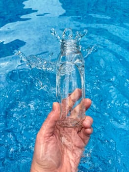 Hand splashing water from clear glass bottle into a blue pool, dynamic motion freeze shot. Clean water concept. High quality photo