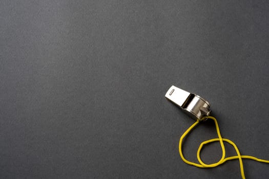 Top view of metal whistle with yellow string on dark gray background