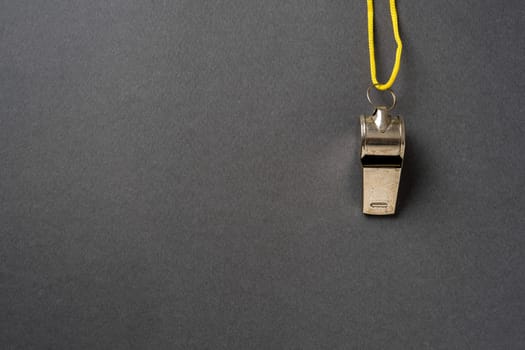 Top view of metal whistle with yellow string on dark gray background