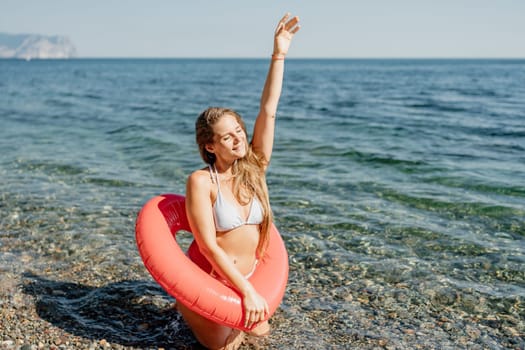 A woman is sitting in the water with a red inflatable ring. She is smiling and waving