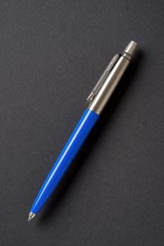 Blue plastic and metal ballpoint pen on dark gray isolated background