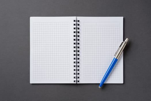 Checkered and spiral notebook on a dark gray table with a ballpoint pen next to it