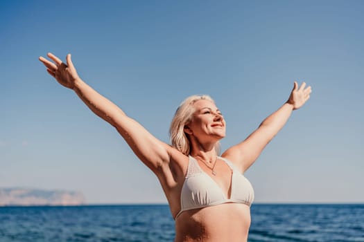 A woman is standing on the beach with her arms outstretched, smiling and enjoying the beautiful blue ocean