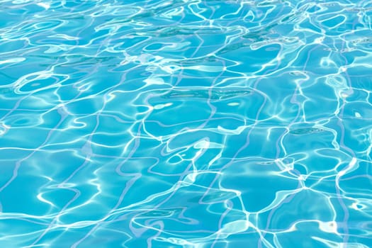 Blue swimming pool water surface and ripple wave background. Summer abstract reflection caustics in swimming pool.