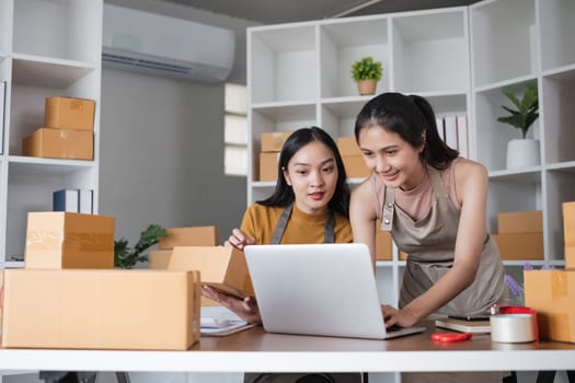 Two businesswomen managing online orders with laptop in office. Concept of e-commerce and teamwork.