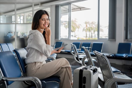 Young woman waiting at airport with luggage and tablet. Concept of travel and technology.