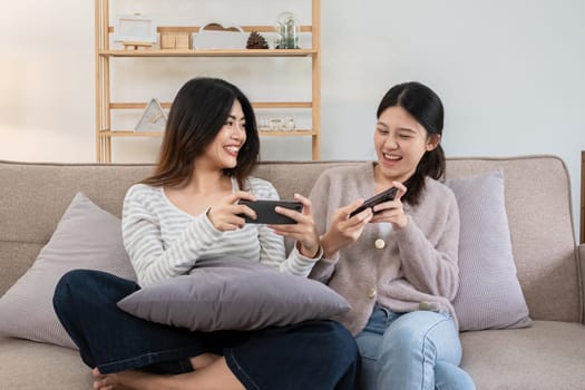 Two young women playing games on smartphones together at home. Concept of friendship and technology.