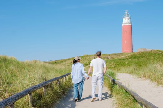 A couple leisurely walks along a path near a picturesque lighthouse on a bright sunny day in Texel, Netherlands.