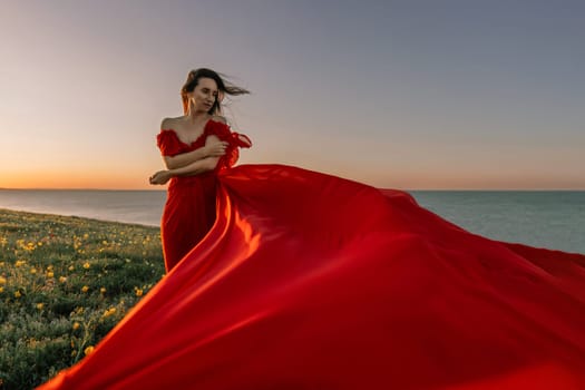 woman red dress standing grassy hillside. The sun is setting in the background, casting a warm glow over the scene. The woman is enjoying the beautiful view and the peaceful atmosphere