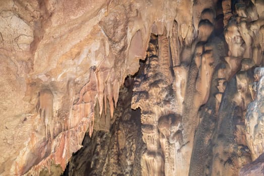 A cave with a lot of rock formations and stalactites hanging from the ceiling. Scene is mysterious and awe inspiring