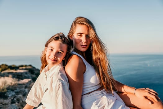 Close up portrait of mom and her teenage daughter hugging and smiling together over sunset sea view. Beautiful woman relaxing with her child.