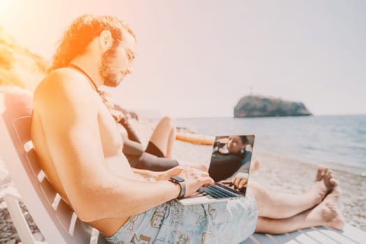 Digital nomad, Business man working on laptop by the sea. Man typing on computer by the sea at sunset, makes a business transaction online from a distance. Freelance, remote work on vacation