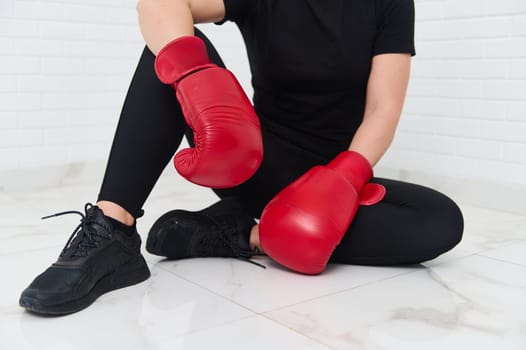 Cropped view of a Caucasian woman in red boxing gloves on a white background. The concept of athletic discipline, sport, combat, martial art. Details on red boxing gloves