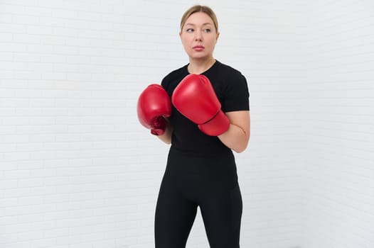 European young woman 30s, fighter boxer in red boxing gloves, standing in fighting position, ready for combat, match, challenge, isolated over white background. Martial art. People and sport