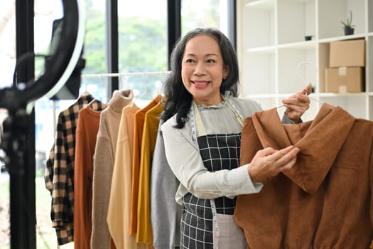 Attractive middle age small business owner live streaming and showing clothing to customer at her shop.