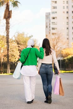 rear view of two unrecognizable women walking in a city park with shopping bags, concept of friendship and urban lifestyle, copy space for text