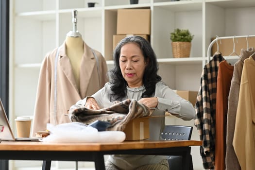 Beautiful middle age female entrepreneur packing product in cardboard box for delivery to customers.