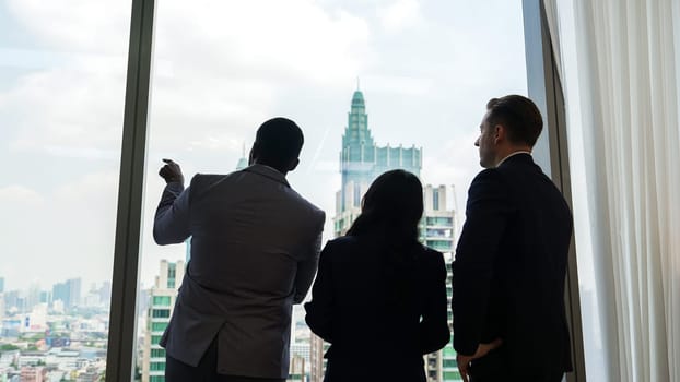 Back view diverse team of ambitious business people standing in ornamented office gazing out window to cityscape skyline. Determination and business ambition drive their career toward to bright future