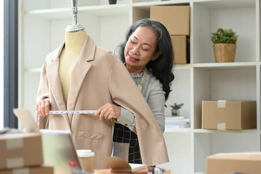 Smiling middle age female tailor measuring a suit on mannequin in her studio.