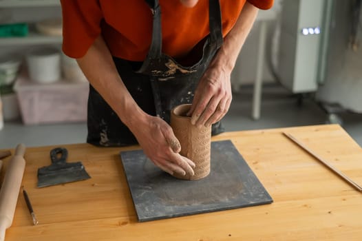 Close-up of a man's hands making a patterned cylinder out of clay