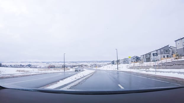 Denver, Colorado, USA-January 26, 2024-The early morning brings a quiet drive through a newly built suburban neighborhood, with fresh snow blanketing the road and houses under a still-dark sky.