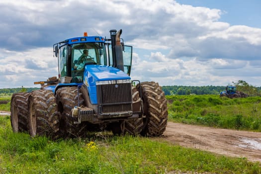 Blue New Holland tractor with double wheels standing near agricultural field at hot sunny day in Tula, Russia - June 4, 2022