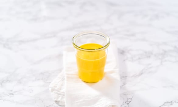 Homemade hollandaise sauce in a glass jar on a marble background.