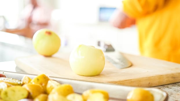 In the welcoming setting of a modern kitchen, a young man continues his dinner preparation process. He's currently involved in slicing yellow onions into rings, prepping them for grilling on an outdoor grill, a crucial step in creating a flavorful meal.