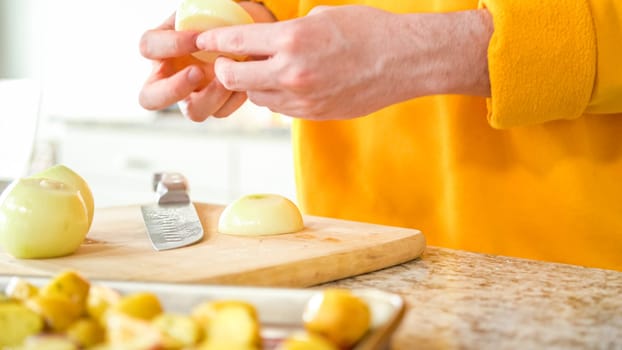 In the welcoming setting of a modern kitchen, a young man continues his dinner preparation process. He's currently involved in slicing yellow onions into rings, prepping them for grilling on an outdoor grill, a crucial step in creating a flavorful meal.