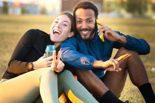 happy young couple using smartphone and sports bottle in hand while looking at camera