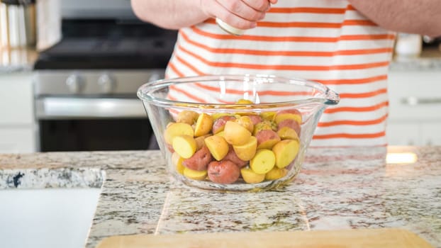 In a sleek, modern kitchen, a young man attentively prepares dinner. His current task involves carefully seasoning small rainbow potatoes in a glass bowl, promising a flavorful meal ahead.