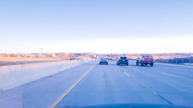 Denver, Colorado, USA-January 26, 2024-Vehicles are lined up during the morning rush-hour on a highway leading from suburban areas towards Denver, with the golden hues of sunrise illuminating the scene.